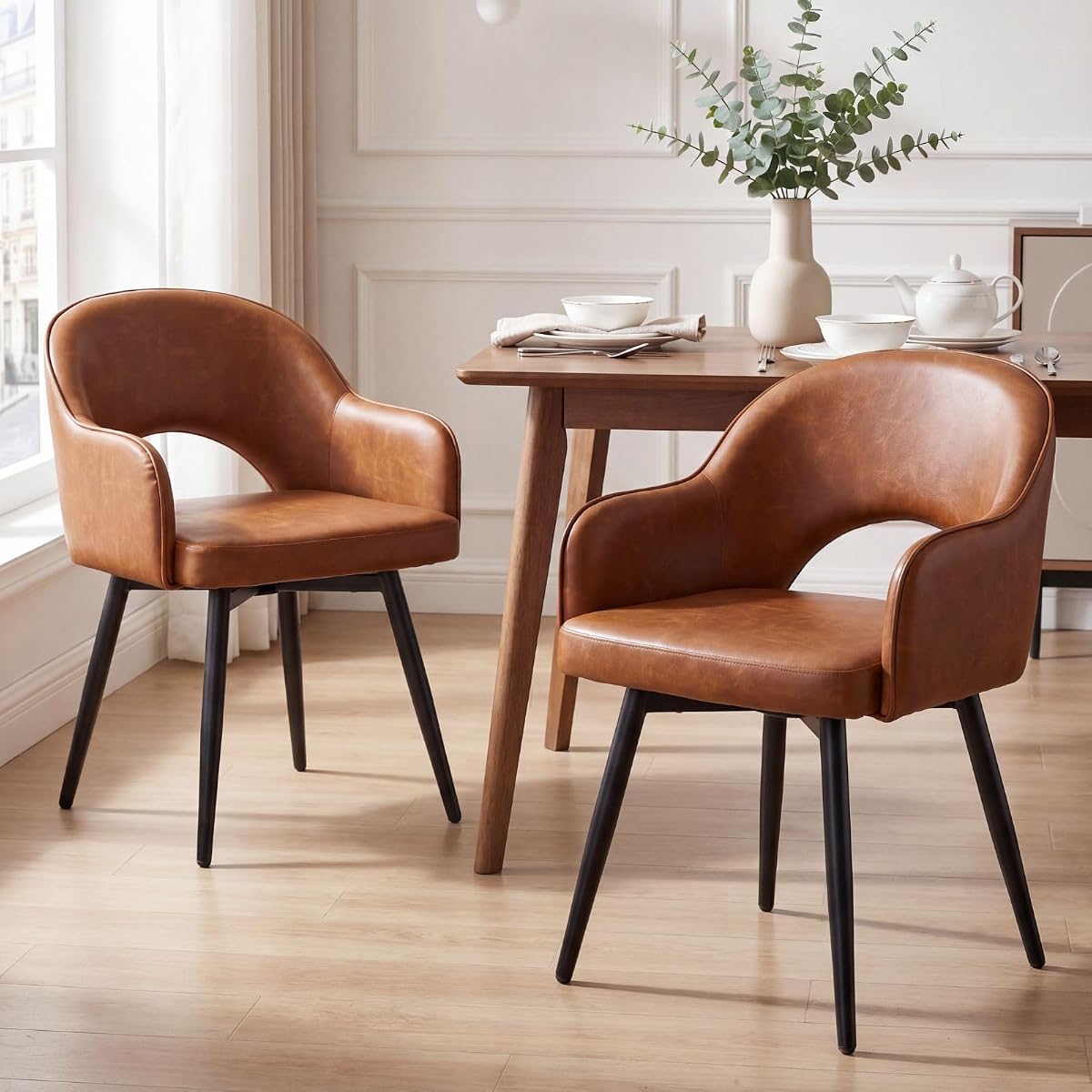 Deux chaises pivotantes en simili cuir marron avec accoudoirs, près d’une table ronde en bois