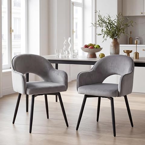 Deux chaises grises en velours, pivotantes, avec accoudoirs et piètement métallique croisé près d’une table ronde.