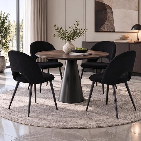 Quatre chaises noires en velours Teddy avec accoudoirs et pieds en métal autour d’une table ronde