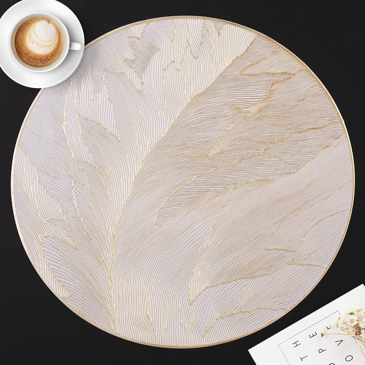 Six sets de table ronds en PVC à motif de plumes dorées, présentés sur une table en bois naturel