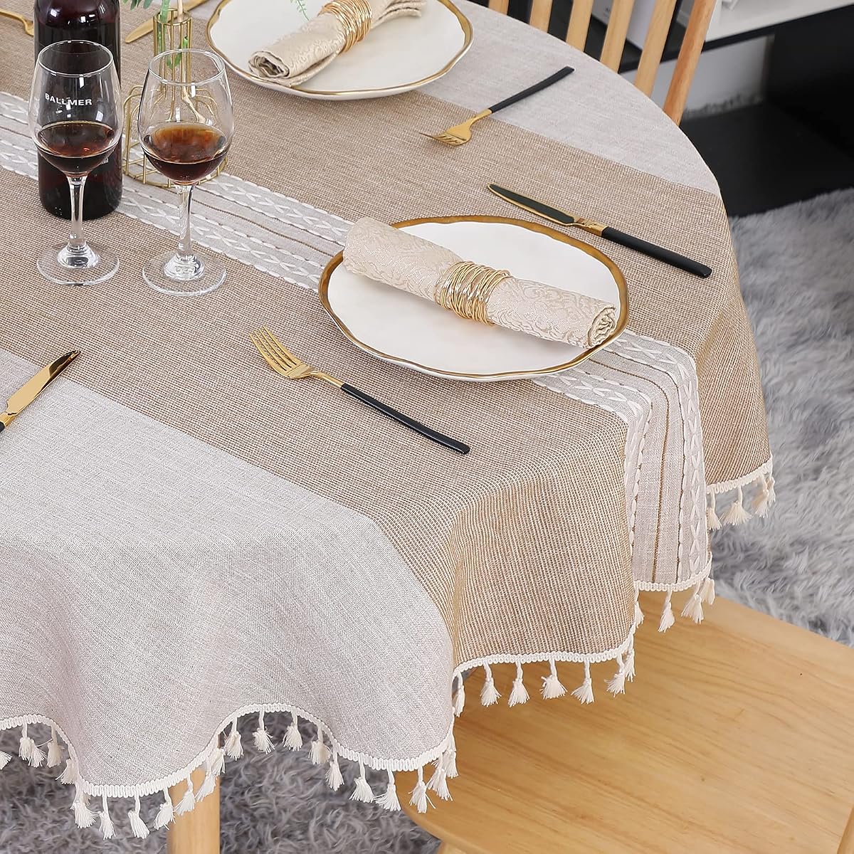 Nappe ronde kaki à bandes brodées et franges, posée sur une table en bois naturel