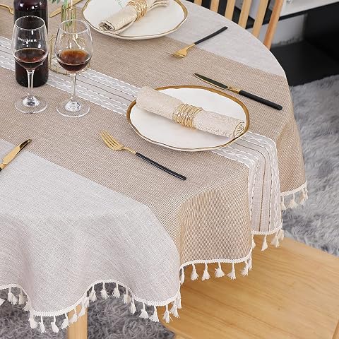 Nappe ronde kaki à bandes brodées et franges, posée sur une table en bois naturel